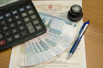 На столе в кабинете лежит заверенная нотариусом  доверенность,  ручка, печать нотариуса, калькулятор и деньги –купюры монеты РФ 