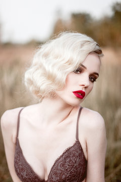 Beautiful and elegant smiling sexy blonde woman with red lips and hair waves wearing beige liingerie posing on the field outdoors summer, retro vintage style and fashion. 