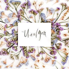 Words "Thank you" written in calligraphic style on paper with blue and purple dried flowers on white background. Flat lay, top view