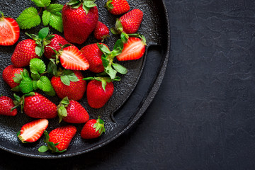 Juicy ripe strawberries on a black cast-iron dish.