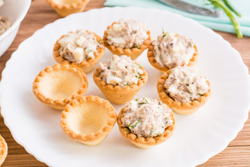 Тарталетки пустые и заполненные салатом из рыбы и яиц на терелке