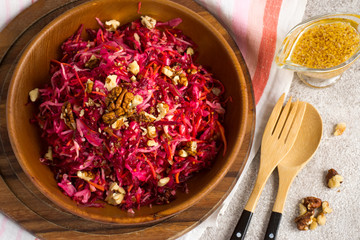Cabbage beetroot carrot salad with nuts  in a wooden bowl closeup.