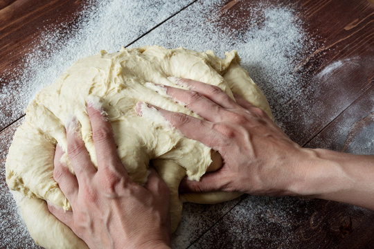 hands knead dough on wooden table