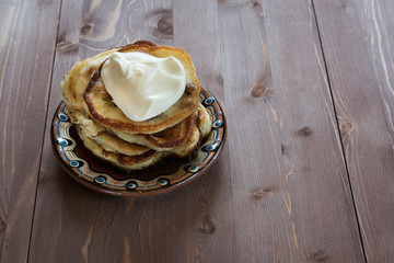 pancakes with sour cream to a painted clay saucer on wooden background