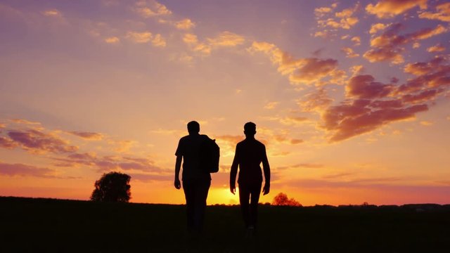 Silhouettes of two men - son and father go together to meet the sunset. Back view. Steadicam shot