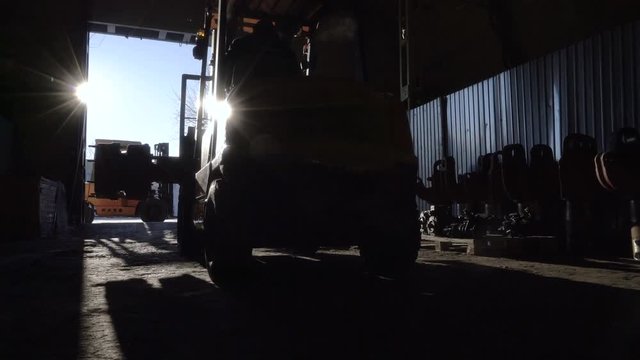 Worker moves a huge part with a telpher. Diesel Forklift Truck leaves the warehouse. Working in the warehouse in winter.
