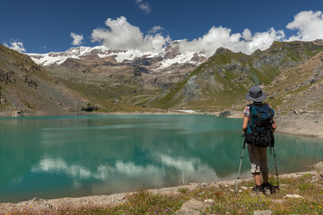 Hiker woman with backpack on mountain lake in Italian Alps