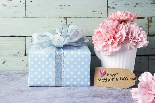 Happy mothers day message on brown paper tag and pink carnation flower in white cup and gift box