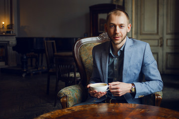 Young man sits and enjoys coffee in the morning. Portrait in the interior