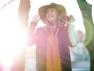 Funny young woman in elegant hat and scarf, walking. Portrait of the charming blonde on the street. Bright sunlight and shading in warm tones