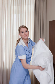 room maid fluffing up pillow, laughing