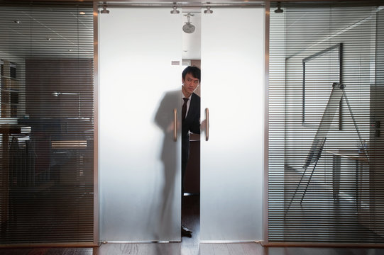 Businessman Peeking Out Of Double Doors