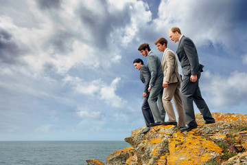 Businessmen peering over cliff edge