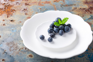 Fresh blueberries on white plate on old rusty blue background. Healthy eating and nutrition concept with copy space.