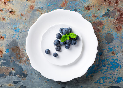 Fresh blueberries on white plate on old rusty blue background. Healthy eating and nutrition concept with copy space. Top view.