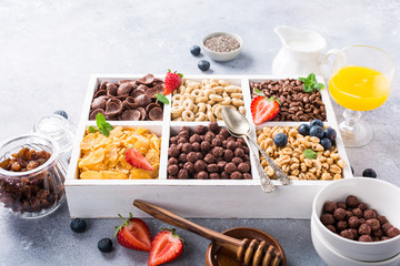 Variety of cold quick breakfast cereals with berries in white wooden box, healthy eating for kids, selective focus.