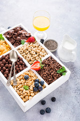 Variety of cold quick breakfast cereals with berries in white wooden box, healthy eating for kids, selective focus.