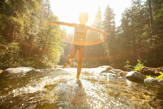 Girl standing in stream with arms outstretched