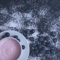 Yoghurt and blueberries lie on a black chalkboard