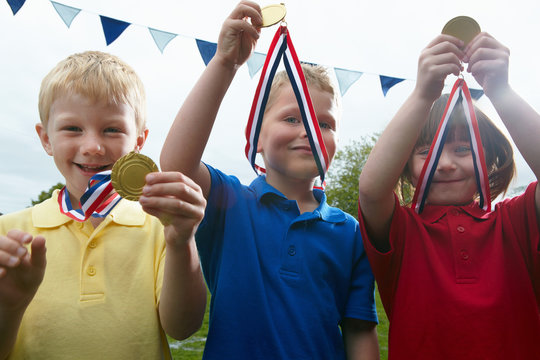 Three children holding sports medals on the school playing field