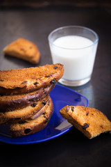 Biscotti or cantuccini cookies with raisins and milk on a blue plate.  Dark grey background