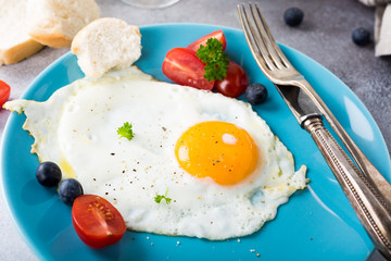 Fried egg on blue plate, tomatoes, blueberries and orange juice. Healthy breakfast concept with copy space.