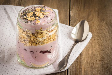 Blueberry yogurt with berries and oatmeal in a glass jar on wooden table. Smoothie and granola.