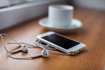 Smartphone, headphones and coffee cup on wooden table