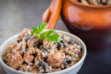 Buckwheat porridge with mushrooms and chicken in a ceramic pot on grey background. Healthy dinner. Top view. Selective focus.