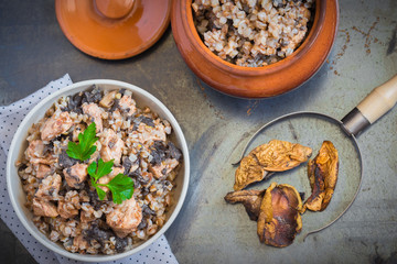 Buckwheat porridge with mushrooms and chicken in a ceramic pot on grey background. Healthy dinner. Top view. Selective focus.