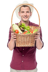 Smiling man shows a basket with grown vegetables in his garden isolated