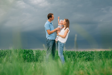 Mother and father holding little daughter standing in the green field. Thunder sky. Happy family concept.