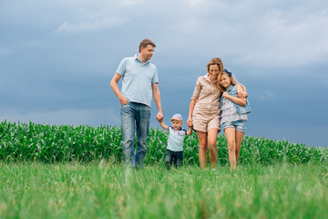 Happy family of four walking through the field. Mother father son daughter Smiling and laughing. Girl with parents and her little  brother