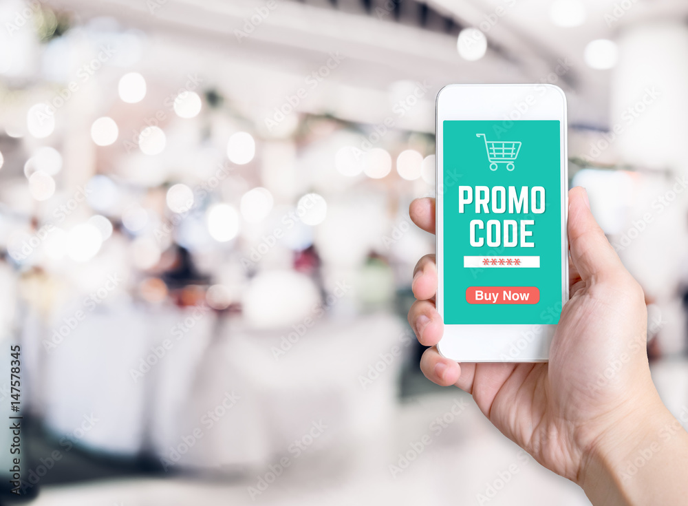 Poster hand holding mobile phone with promo code word with blurred store background with bokeh light ,inter