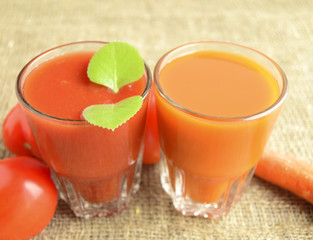 Tomato juice and juice carrot are poured in glasses. Tomatoes and carrots are located a row.