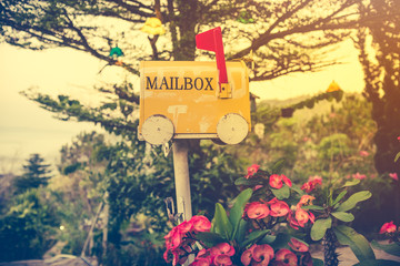 Old yellow stained metal mailbox has red flag raised up to indicate mail has arrived. Outdoor on summer day with bright sunlight at sunset. Vintage effect tone.