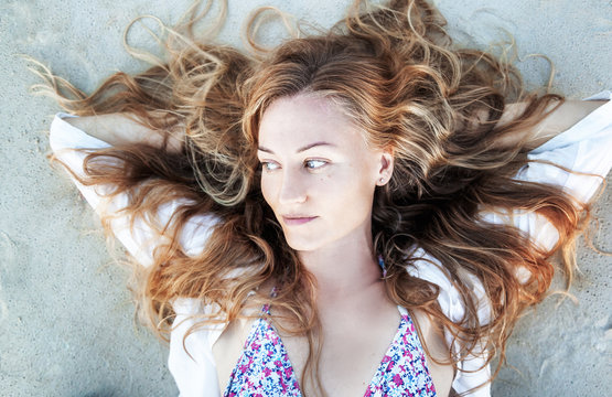 Beautiful young woman with long curly blond hair lies on the sand