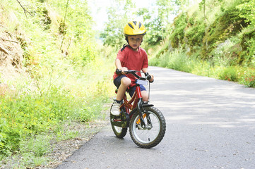 Young boy riding bicycle on a summer day at asphalt road. Bicycle path
