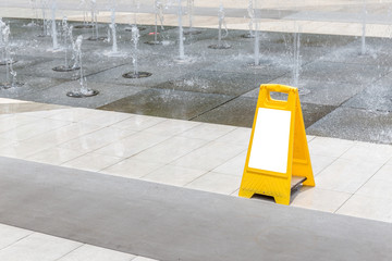 Blank yellow hazard sign alerts for a wet floor in fountain decoration area.
