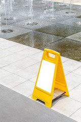 Blank yellow hazard sign alerts for a wet floor in fountain decoration area.