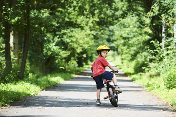 Young boy riding bicycle on a summer day at asphalt road. Bicycle path