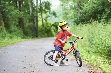 Child boy on a bicycle in the forest in summer. Boy cycling outdoors in safety helmet. Sun flare effect added