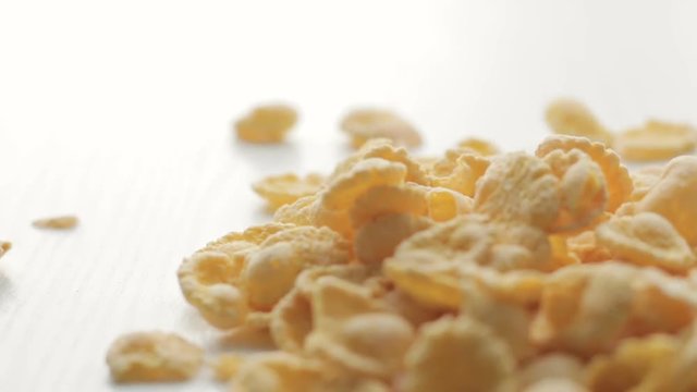 Footage From golden cornflakes falling on white table with soft focus on middle ground
