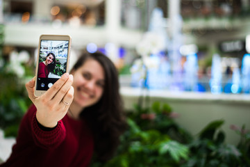 woman taking selfie in mall in front of flower