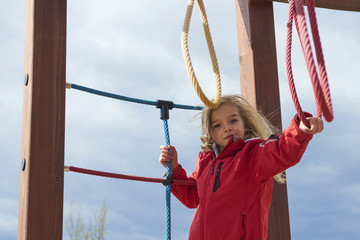 Childhood, leisure and people concept - happy little girl on children playground climbing 