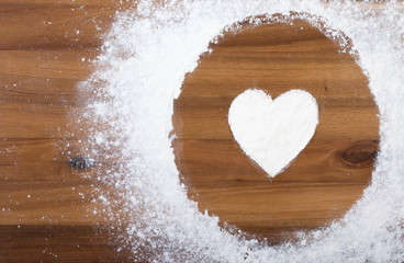 White flour with shape of heart in circle on a wooden cutting board. Top view, close up
