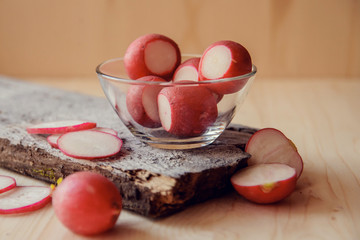 Red radish in clay cup on wooden table with scarf, closeup