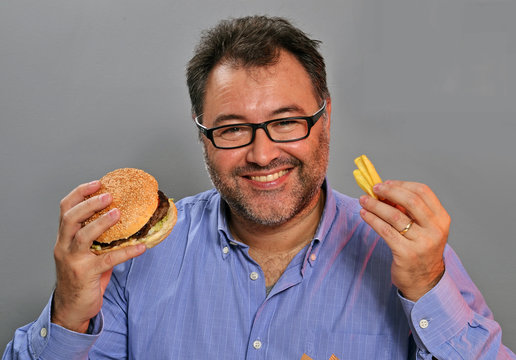 Hombre gordo feliz comiendo hamburguesa y patatas fritas.