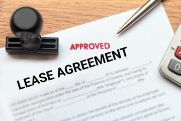Approved lease agreement document with rubber stamp and calculator on wooden desk.