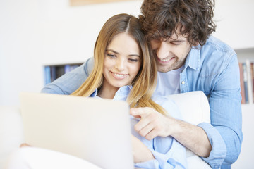 Fototapeta premium Spend time together. Shot of a lovely young couple sitting at home and relaxing. Smiling young woman browsing on the internet at laptop with her handsome boyfriend.
